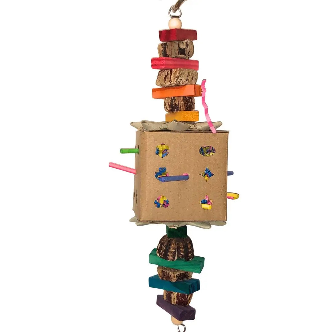 A colorful bird toy made from a cardboard box with wooden blocks, natural wood pieces, and pods