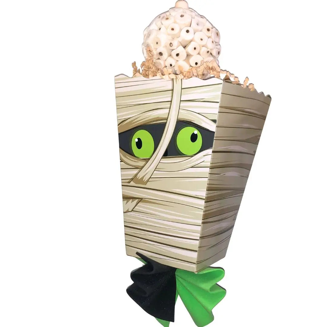 A mummy-themed popcorn bucket Halloween decoration with green monster eyes, beige wood-grain wrapping, a green foam, and a cluster of 3 sola balls