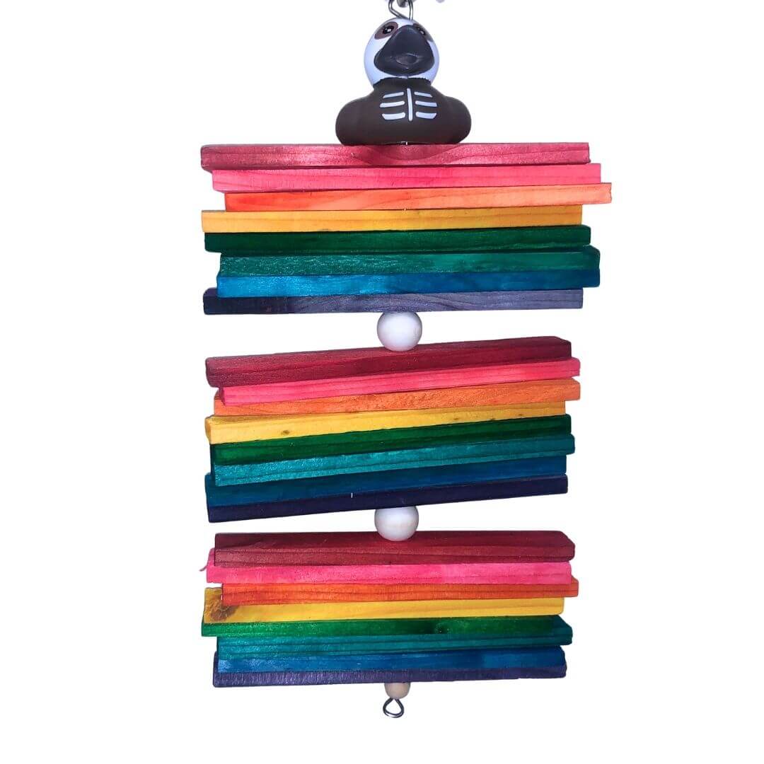 A rainbow wooden bird toy with stacked colorful wooden bars in pink, orange, yellow, green, blue, and purple, hanging from a halloween theme duck. 
