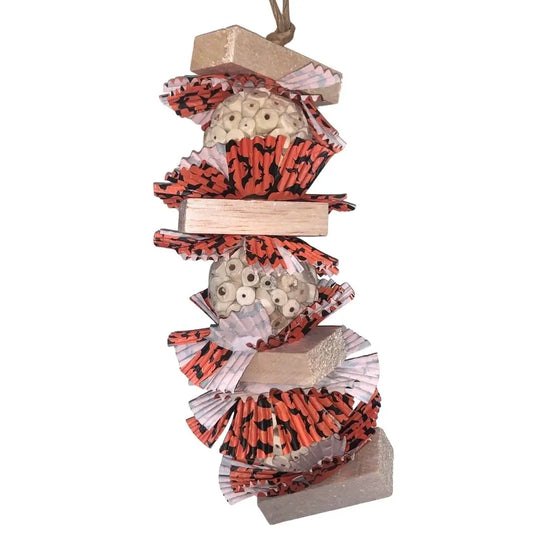 A hanging bird toy made from stacked natural wood blocks, patterned orange and black paper cups, and sola balls on a plain white background.